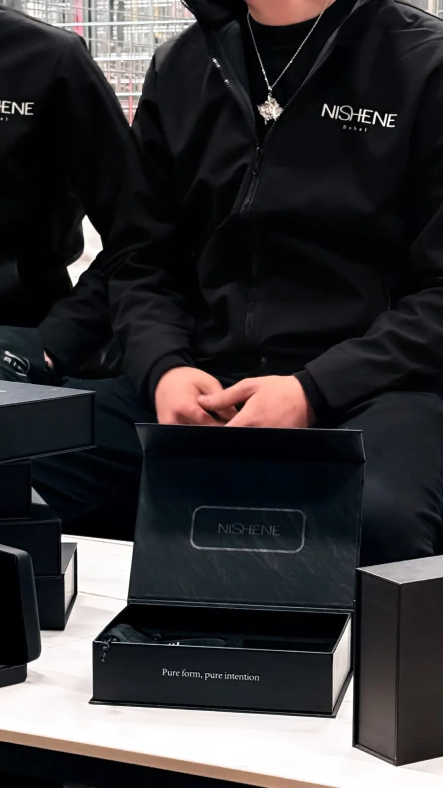 Deux membres de l'équipe NISHENE en veste noire, un collier au cou, devant un coffret ouvert